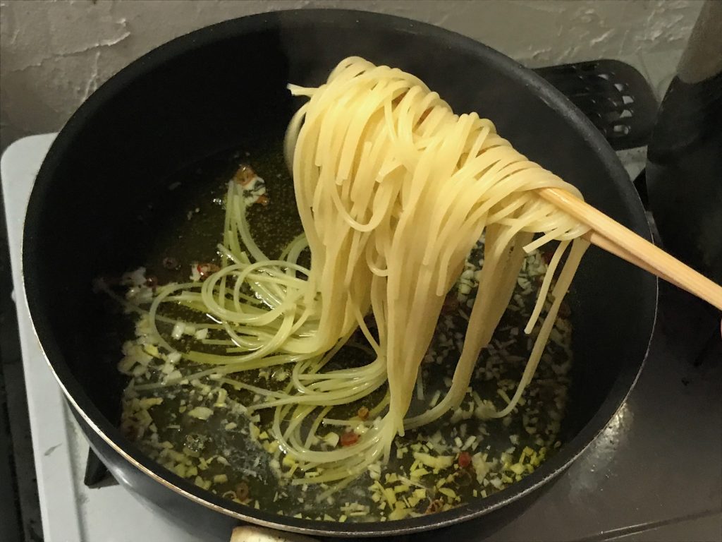 ⑦ 規定時間より短めに茹で上げたスパゲティを（湯切りせずに）箸ですくってフライパンに直接入れて中火にしてかき混ぜる